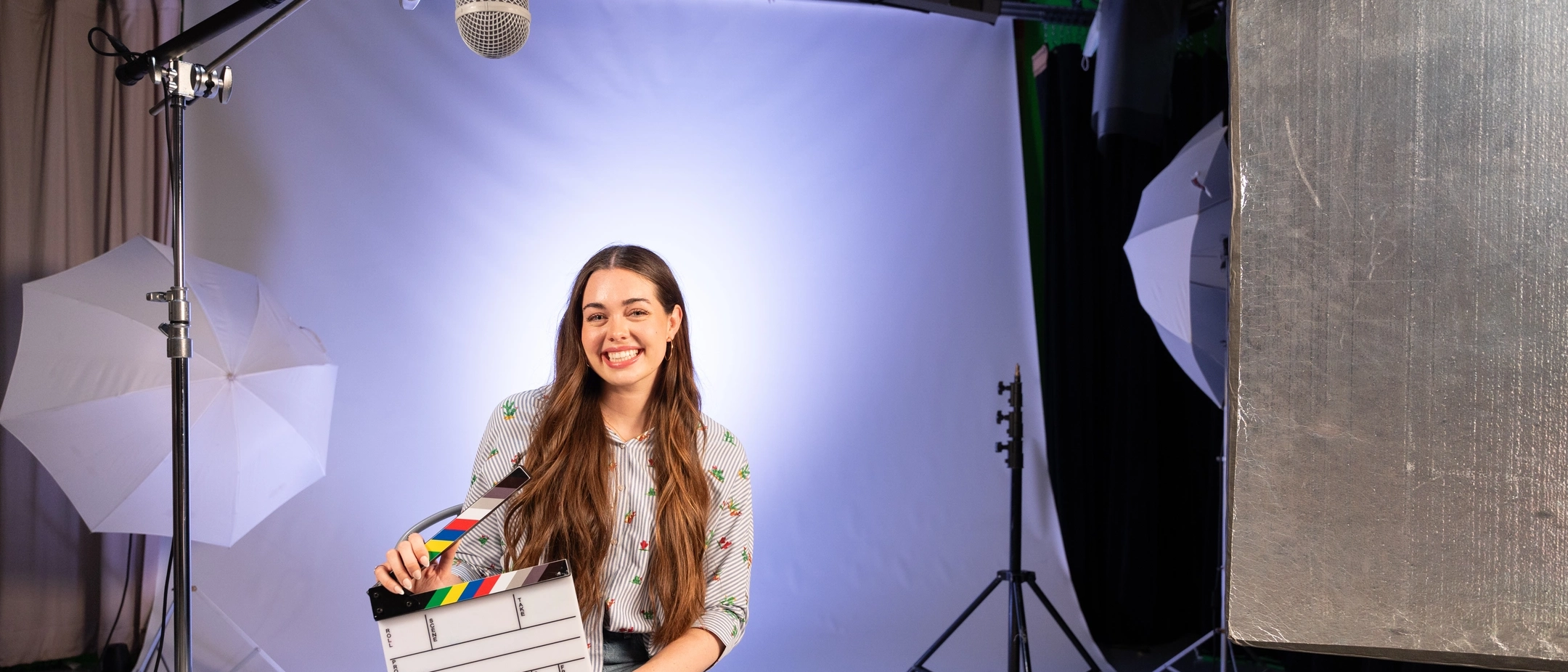 person sitting and holding a movie clacker on their lap within studio environment