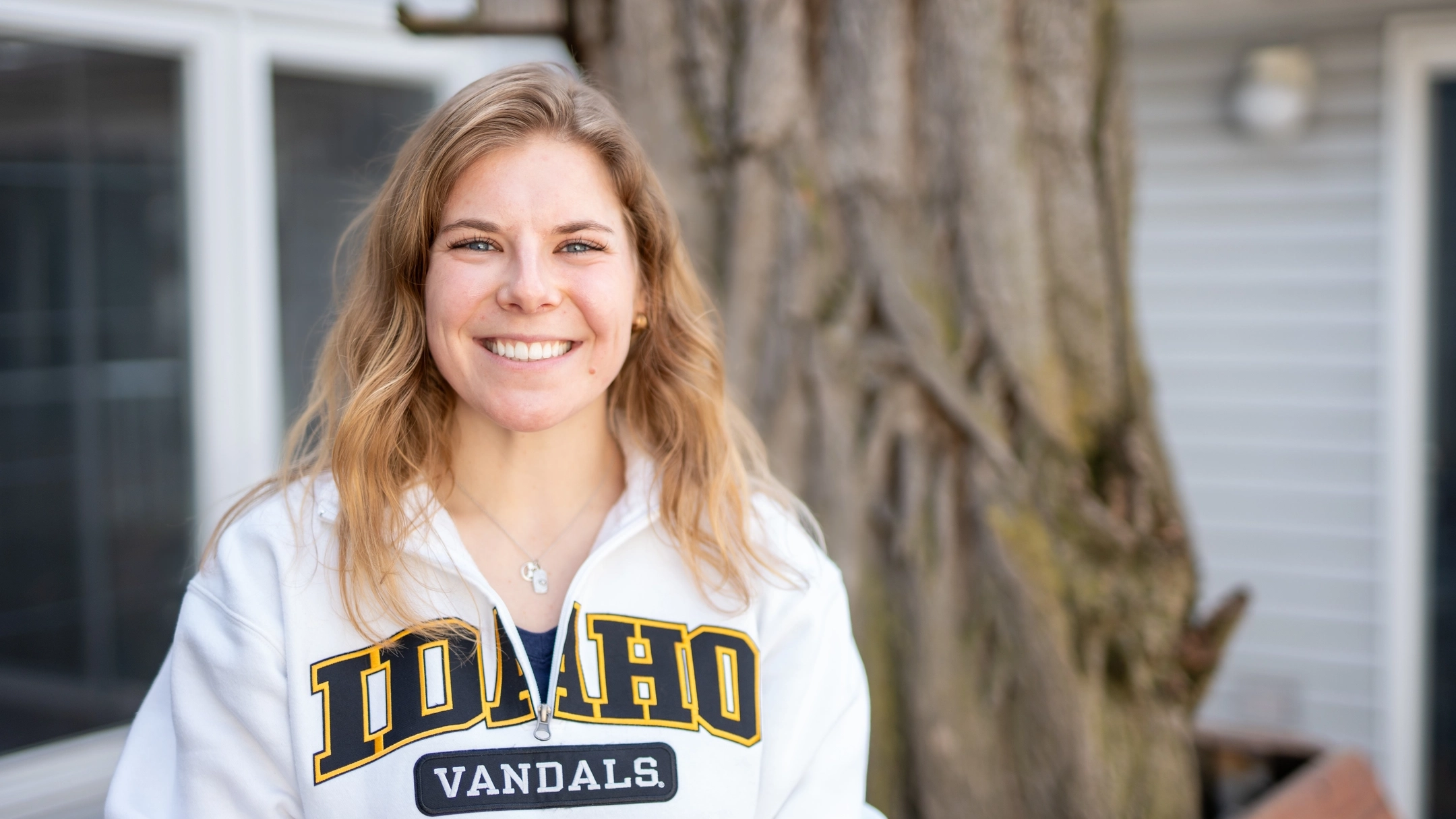 Closeup photo of woman wearing white U of I sweatshirt with large tree in background.