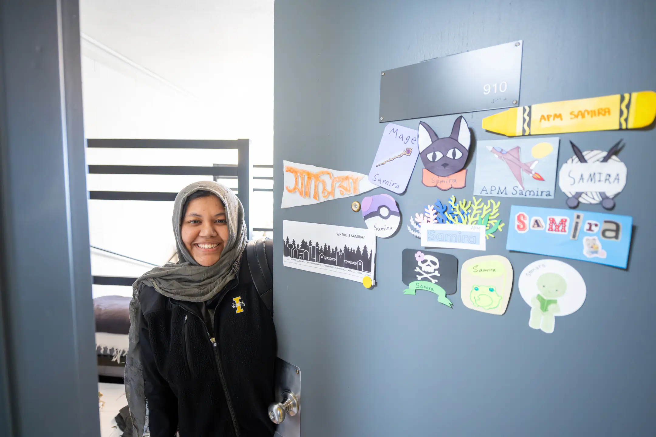 A female student smiles while standing in the open doorway of her newly renovated residence hall room.