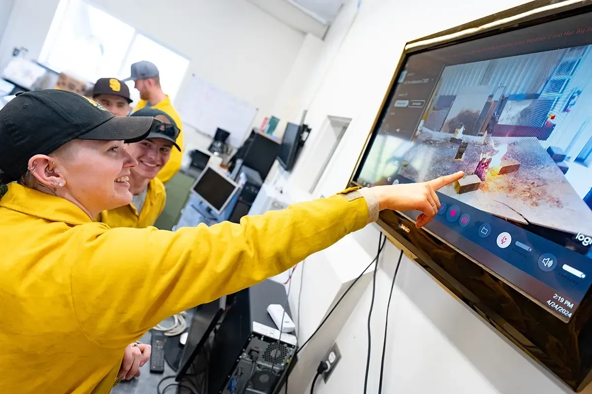 Student points at television recording simulated wildfire