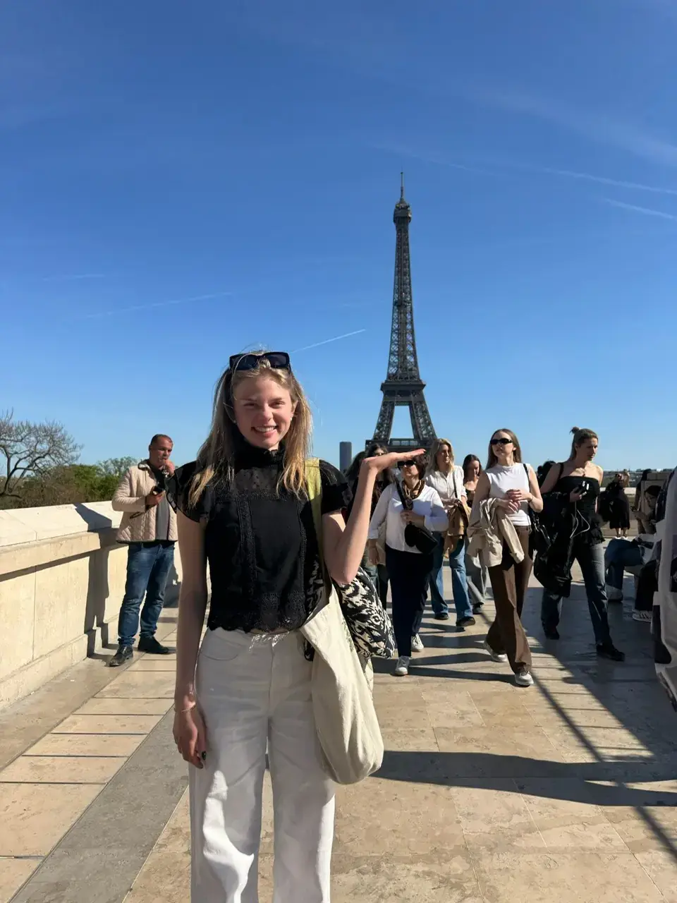 Woman wearing black shirt and white pants standing in front of the Eiffel Tower.