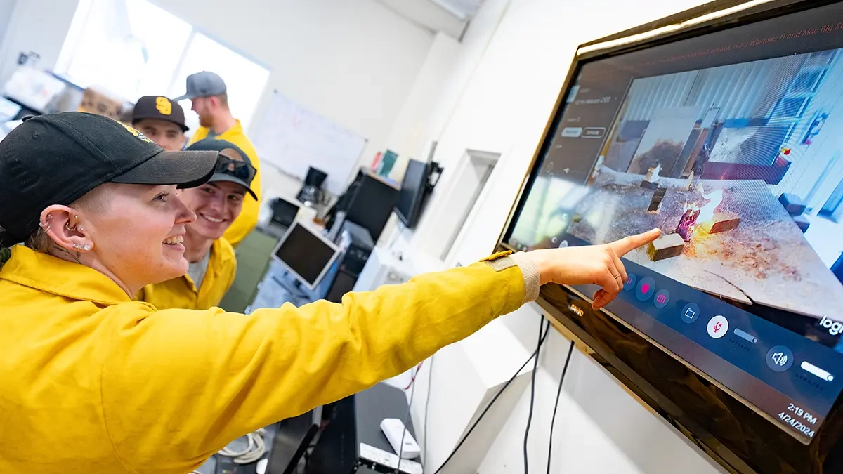 Student points at television recording simulated wildfire