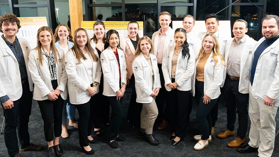 a group of students in white lab coats smile in front of project presentation display boards