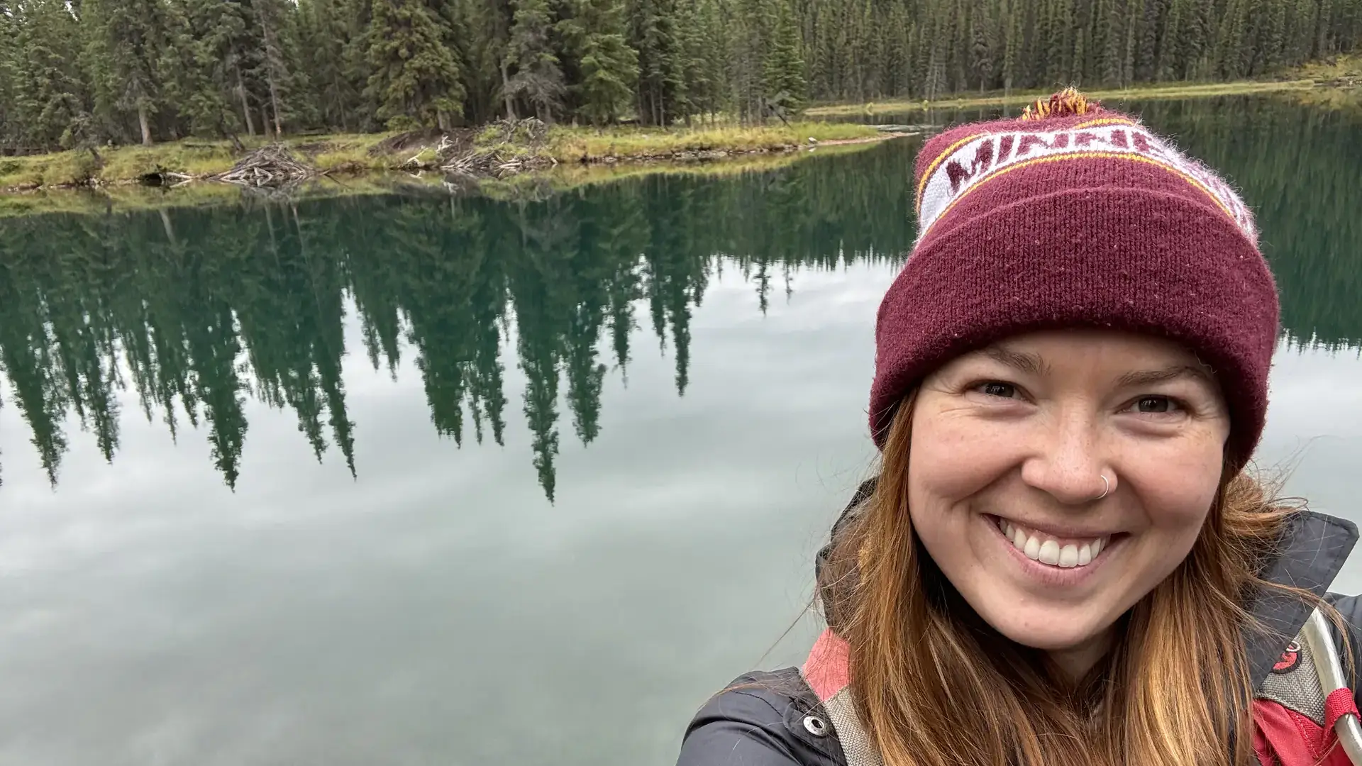 A woman stands by a mountain lake.