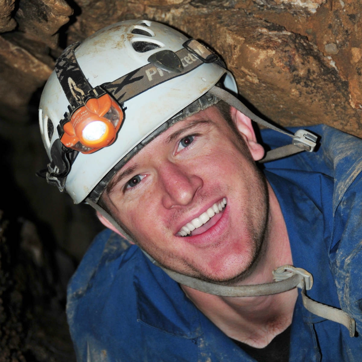A man inside a cave wearing a helmet with a light on it