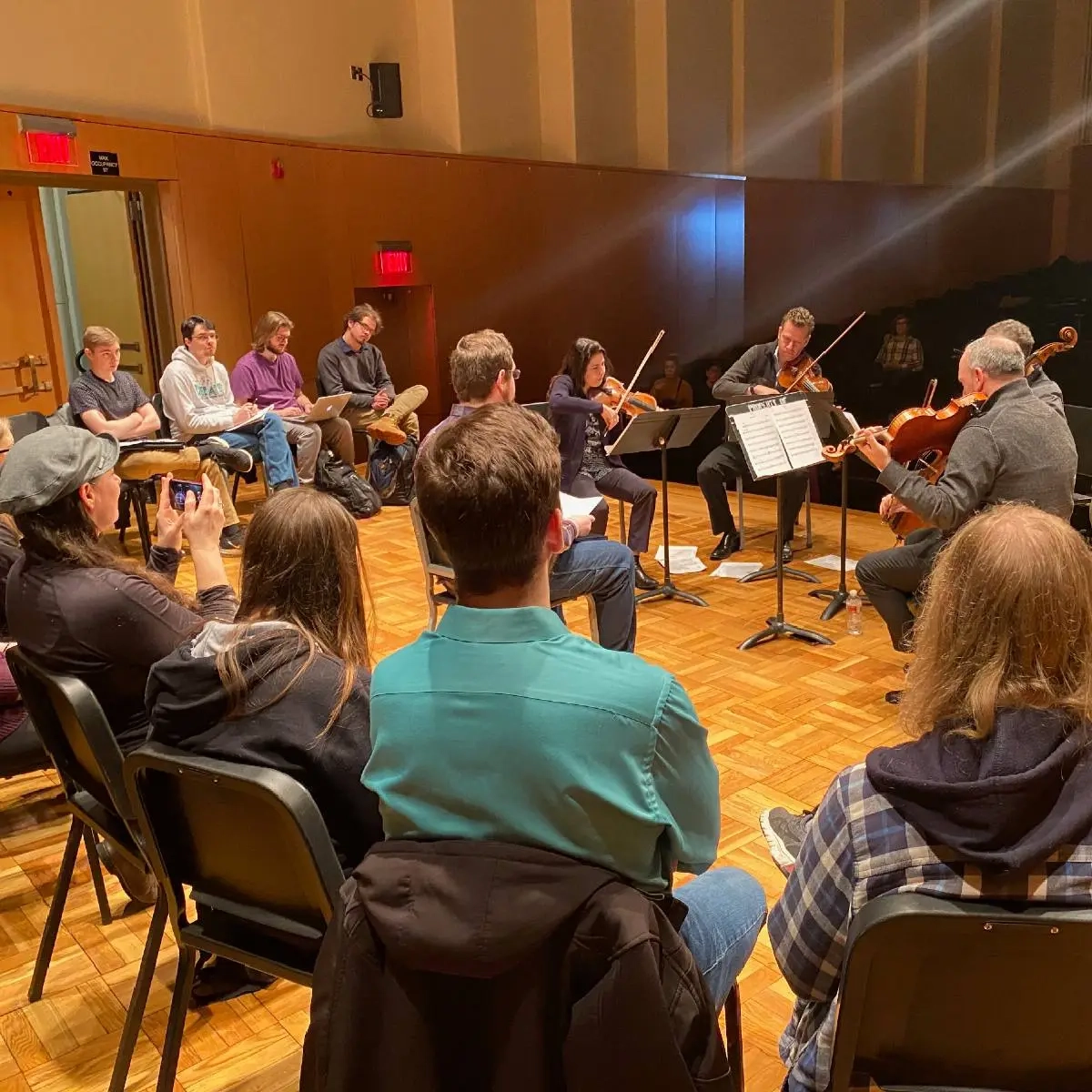 People sitting in a circle around a group playing string instruments