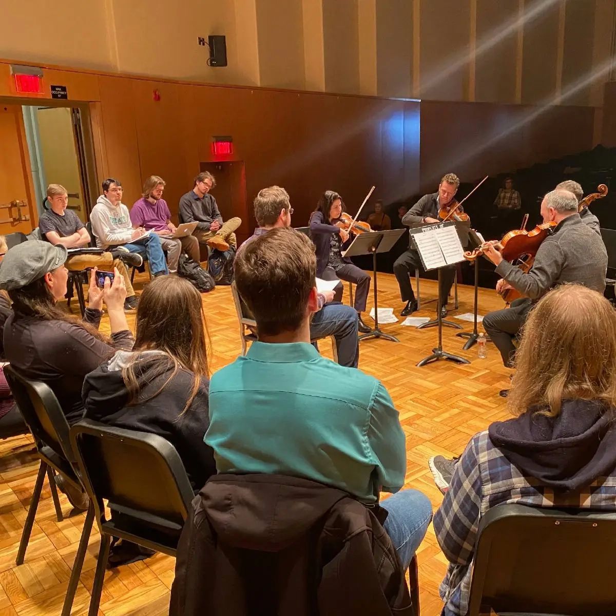 People sitting in a circle around a group playing string instruments