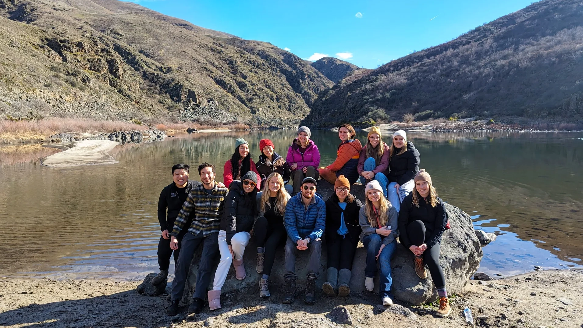 A group of medical students sit in front of a lake and mountains