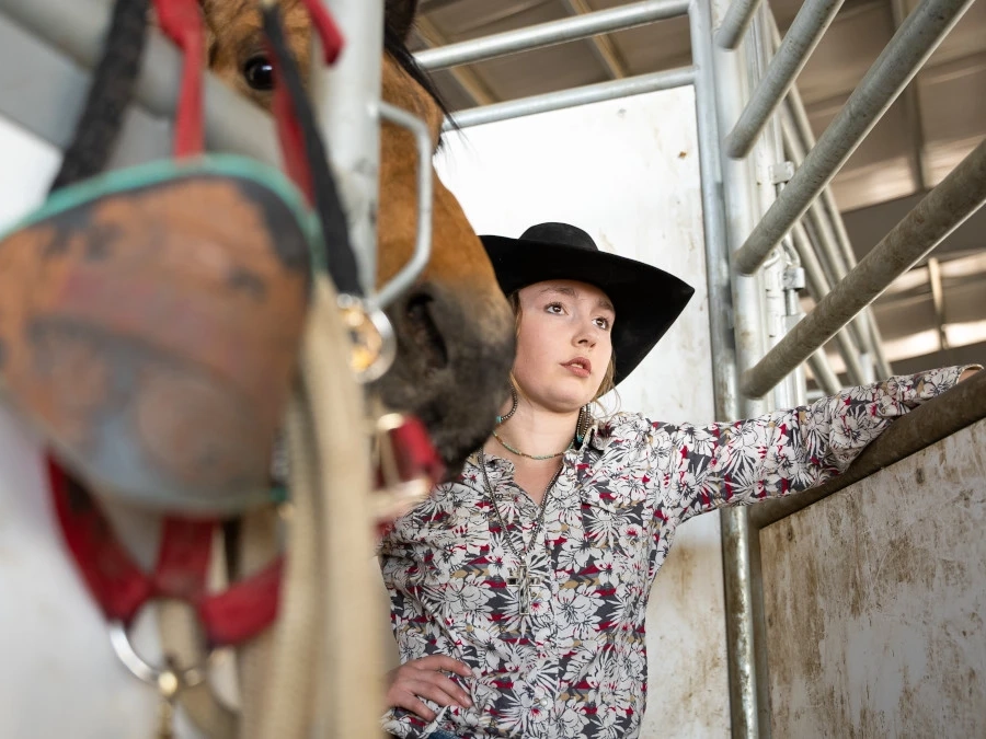 Woman stands in horse stall near horse riding equipment