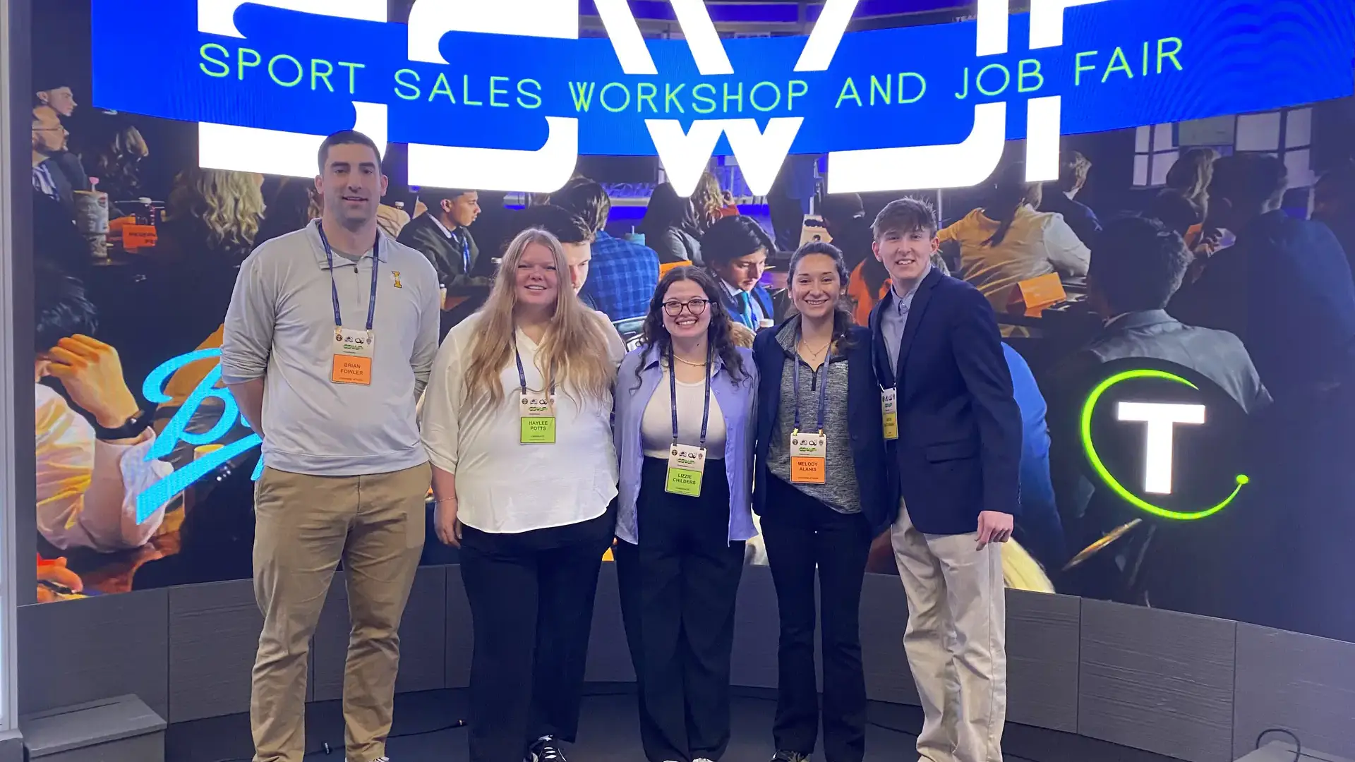 Lizzie Childers, center, with fellow students and two faculty stand in front of a Sports Sale Workshop and Job Fair sign. 