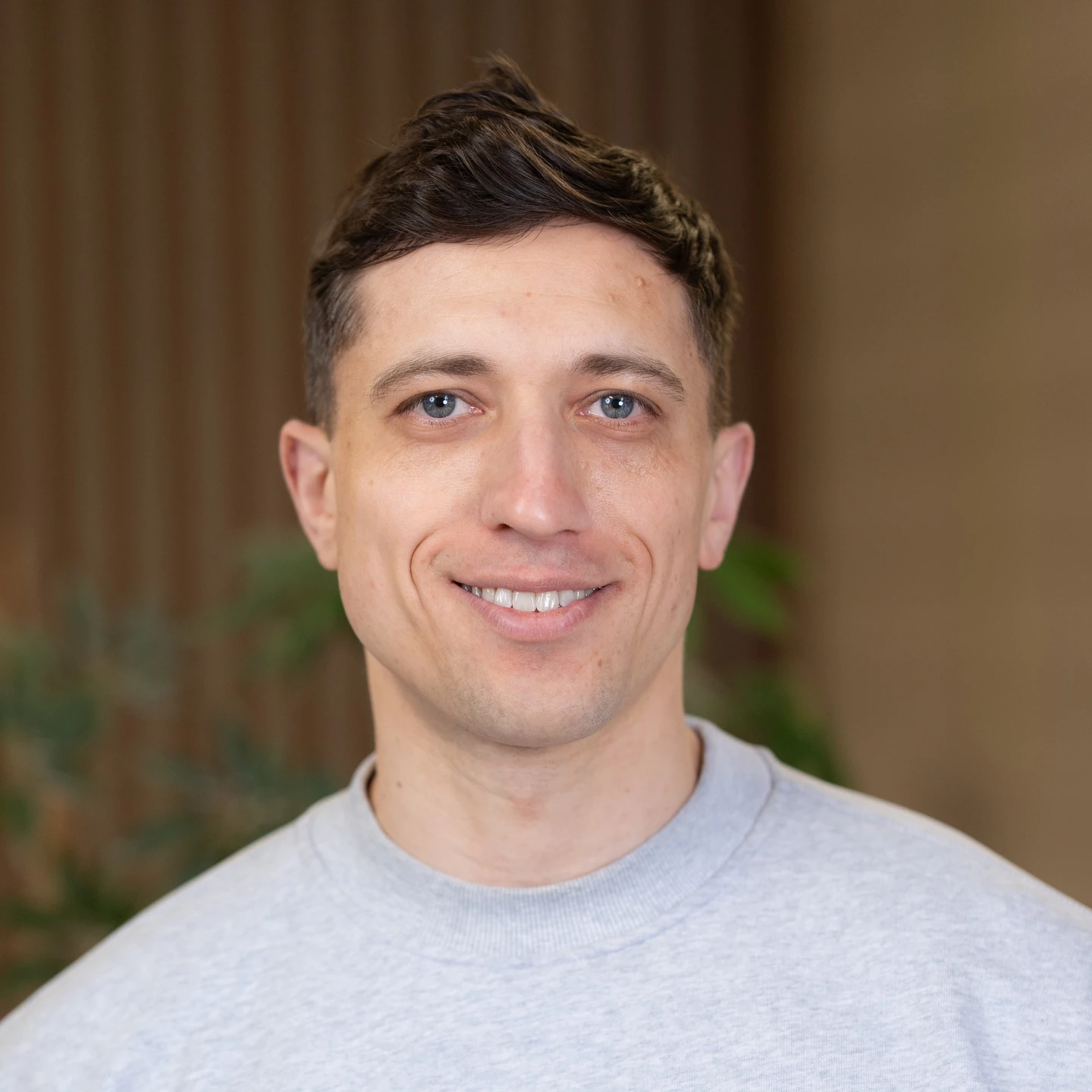 A headshot portrait of a man in a grey crewneck