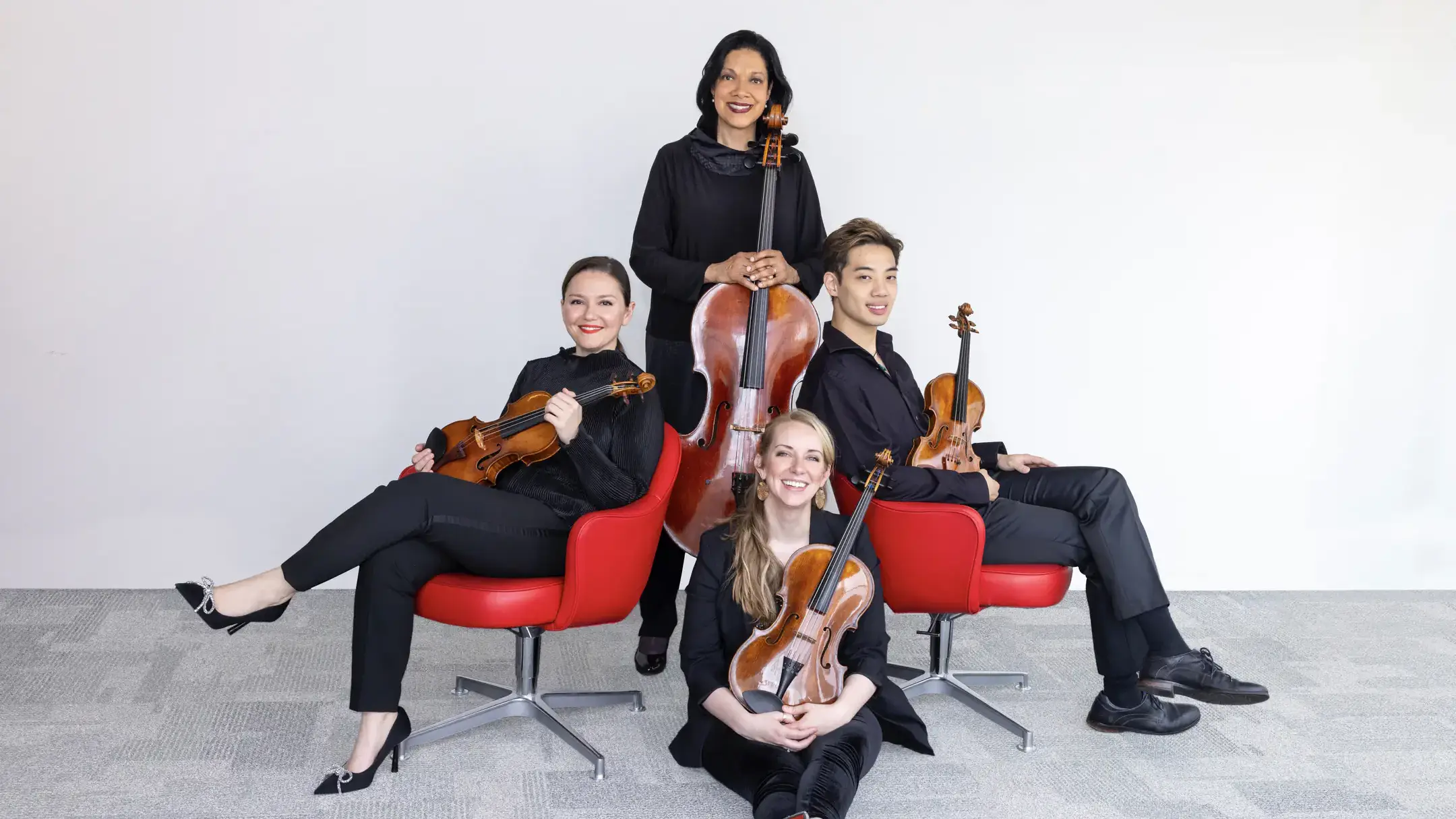 Four musicians holding their instruments, seated to form a plus sign for a group photo.