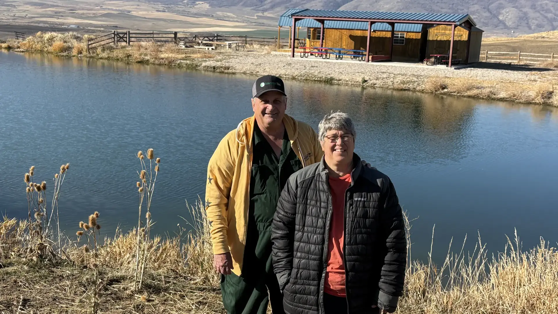 Two people stand in front of a small body of water.
