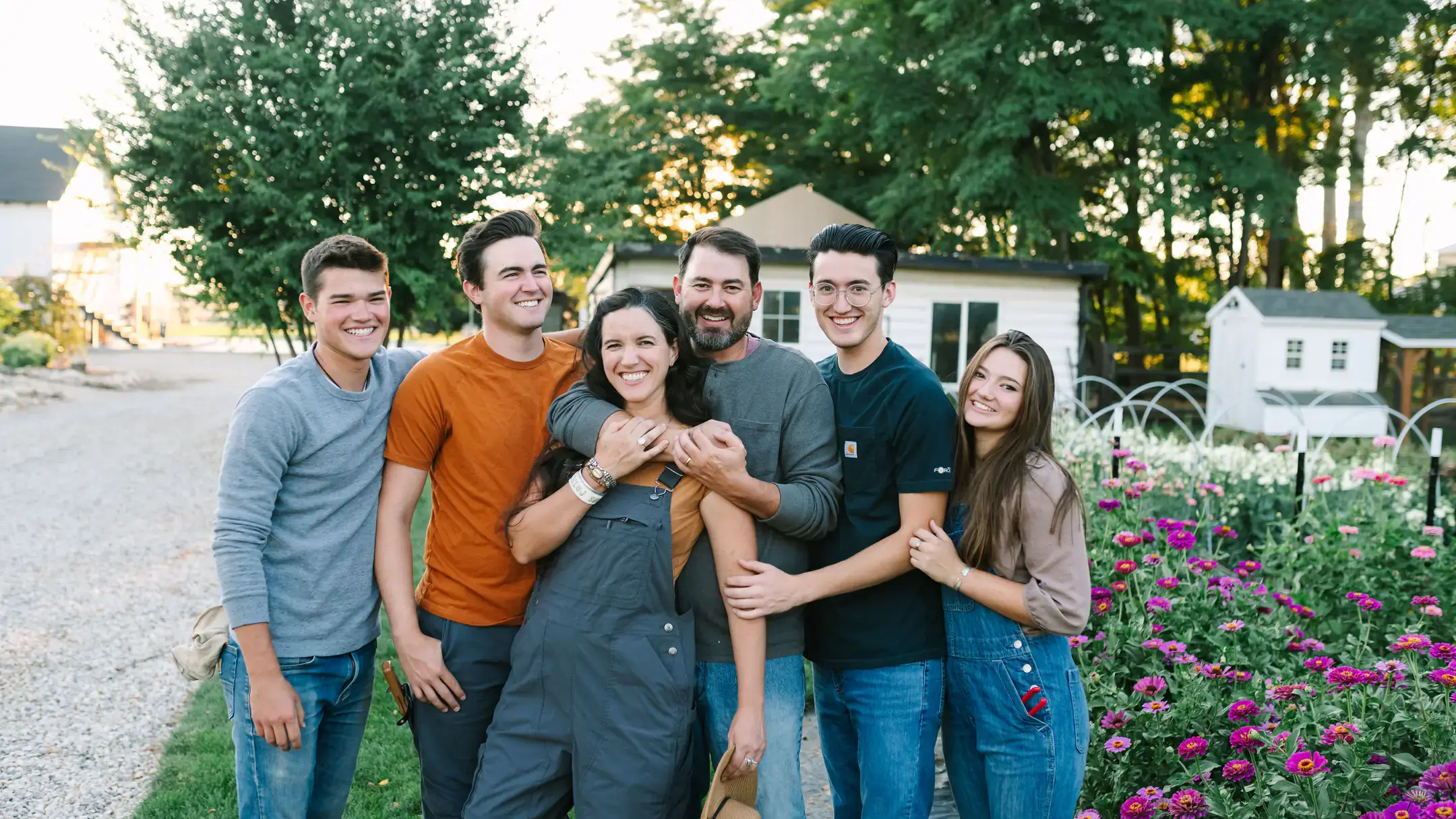 A group of men and women hugging with a flower garden in background