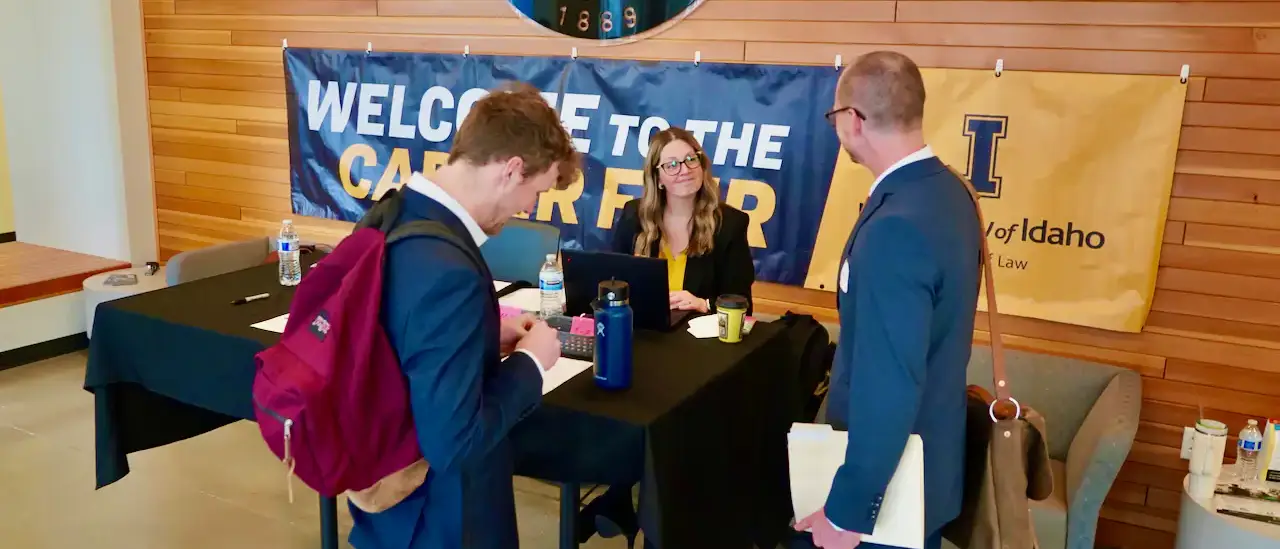 Two men talking to a woman who is sitting behind a check-in desk.
