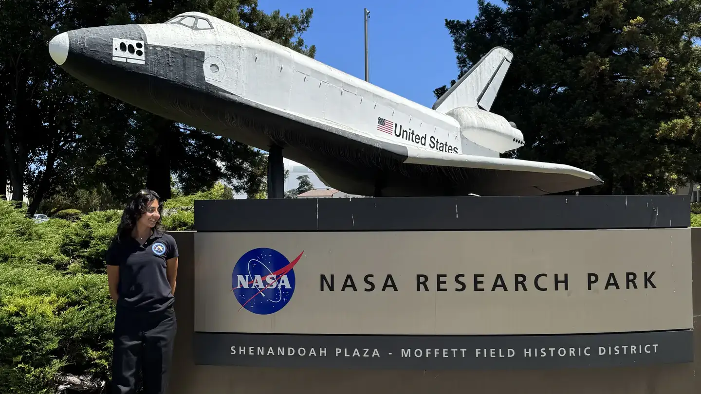 A visitor stands near the entrance of NASA Research Park, featuring a space shuttle model displayed outdoors.