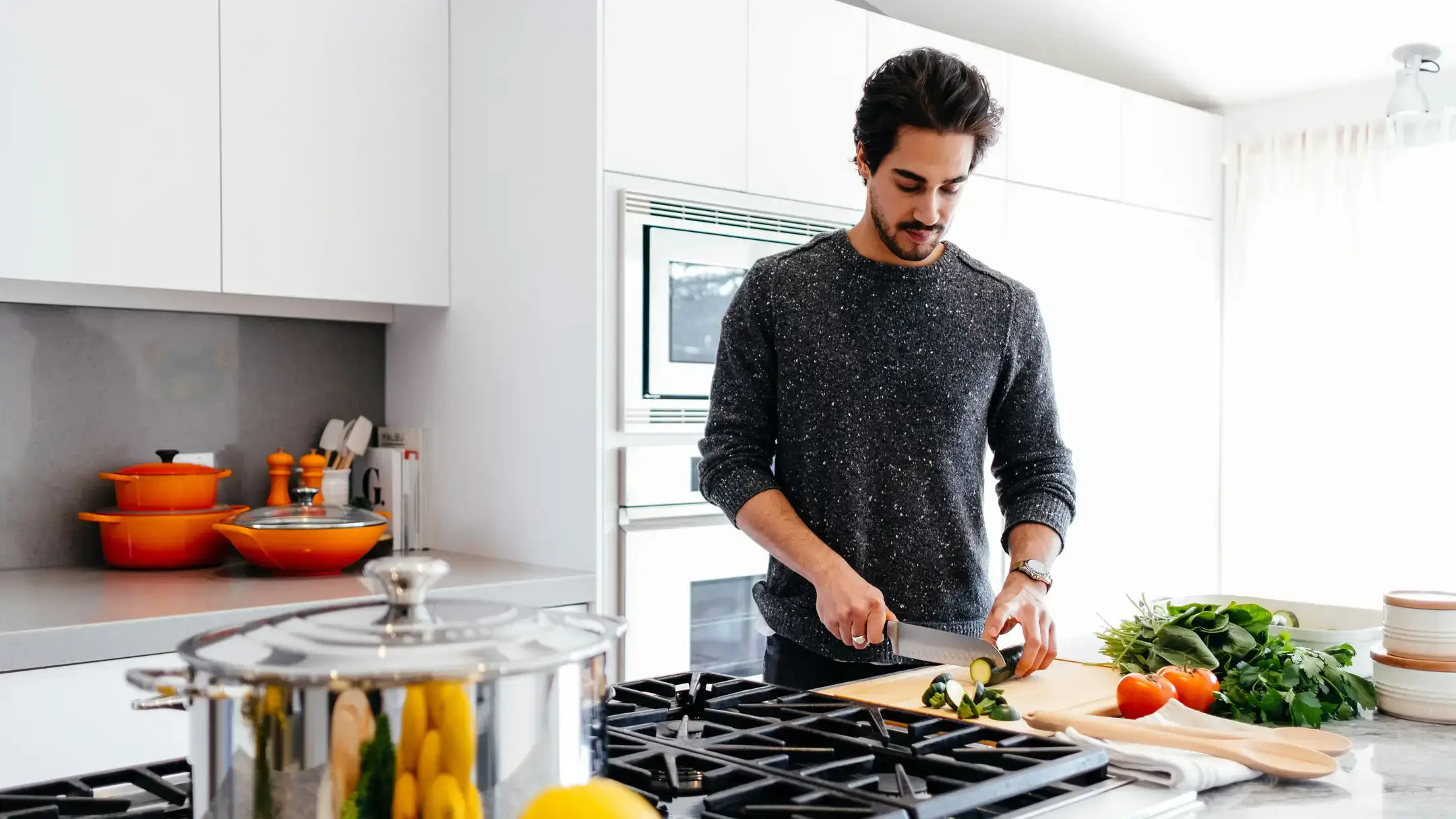 A person cutting vegetables on a board in a modern kitchen with various utensils and cookware on the counter.