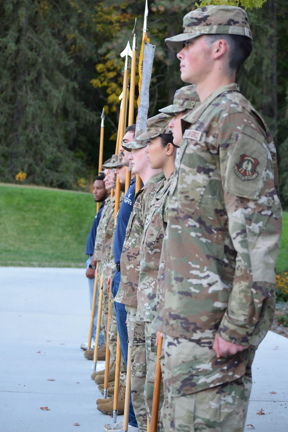 A row of Air Force cadets holding guidons with trees in background.