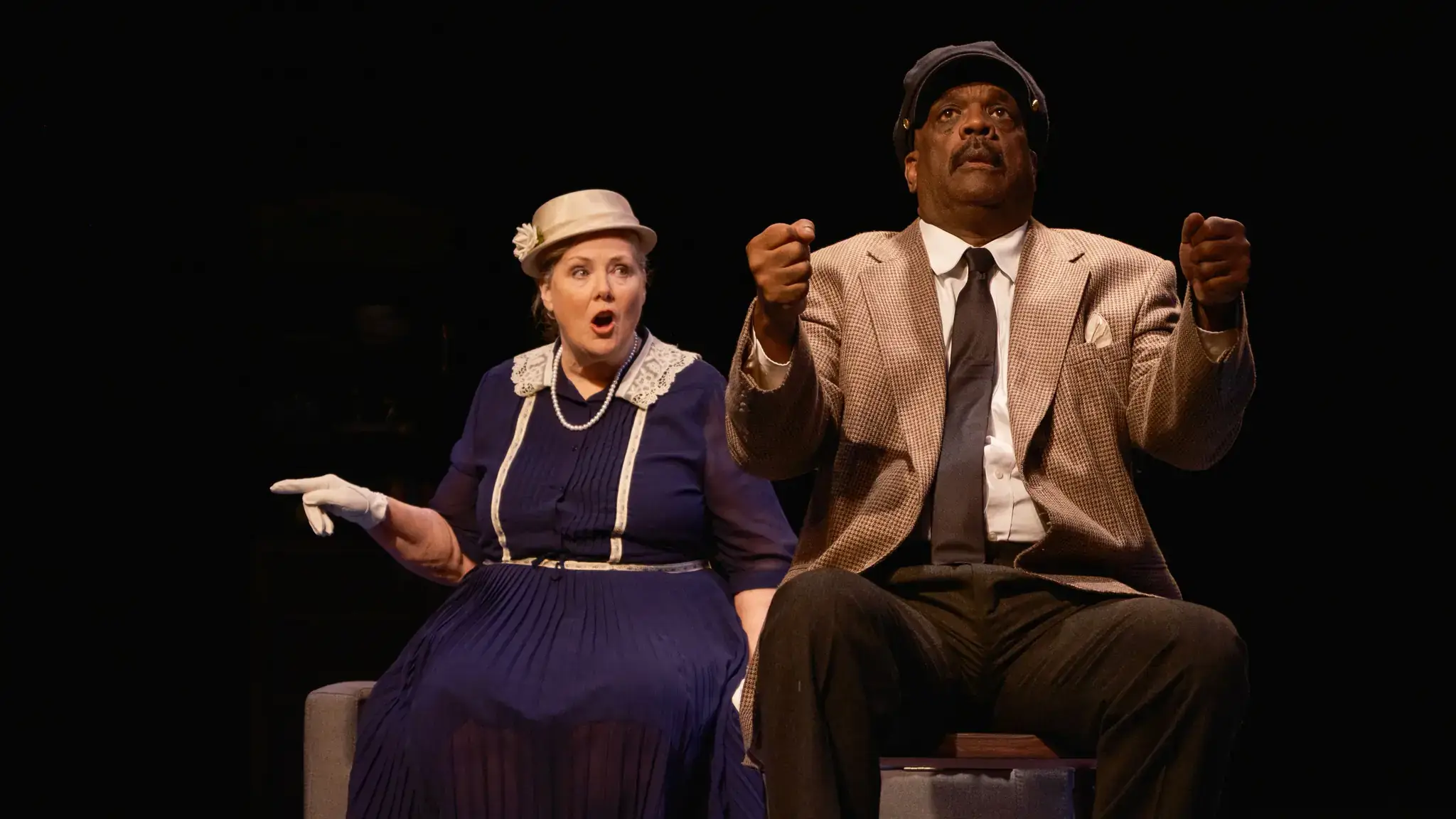 A white woman and Black man pretending to drive in a car.