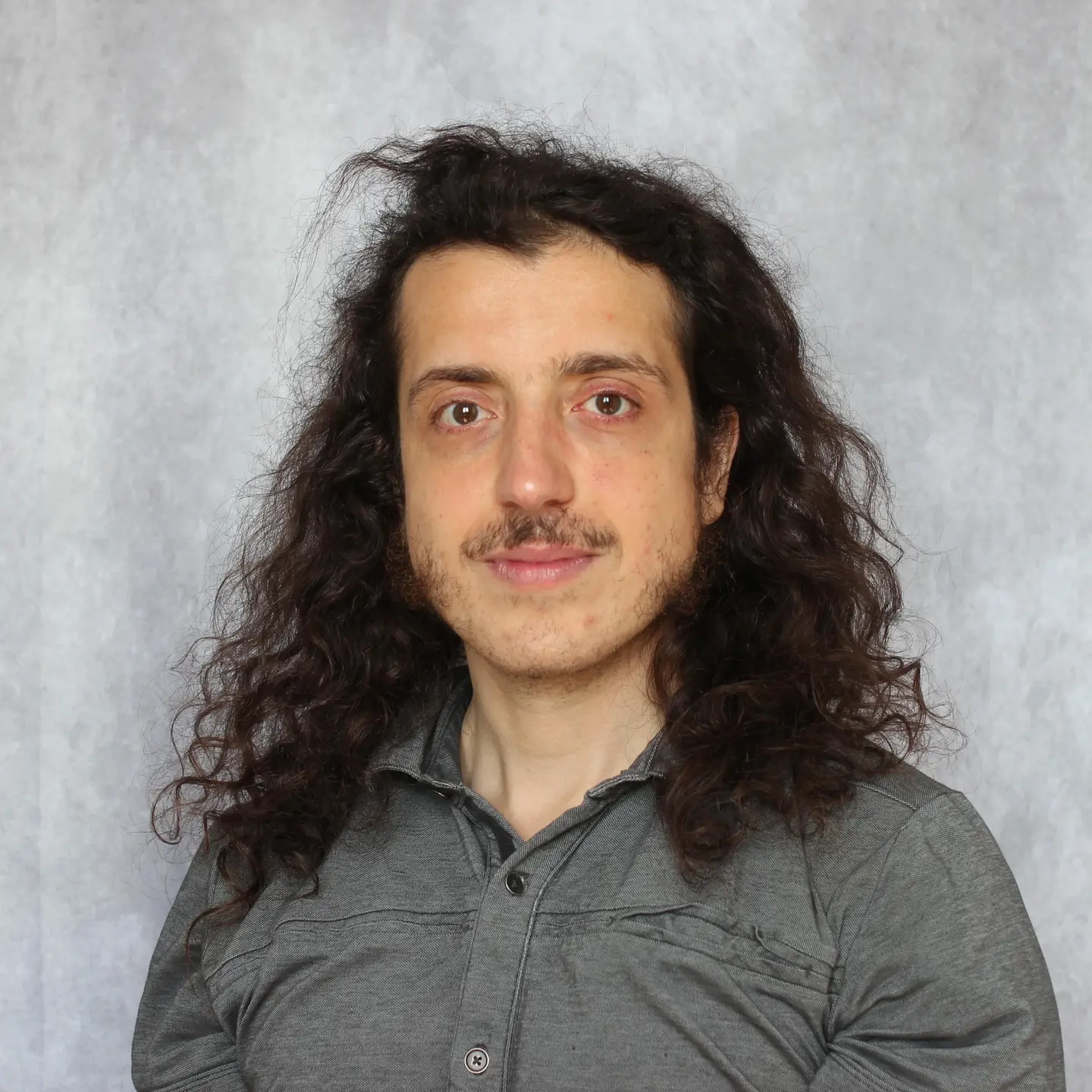 Portrait of a man standing in front of a grey backdrop.