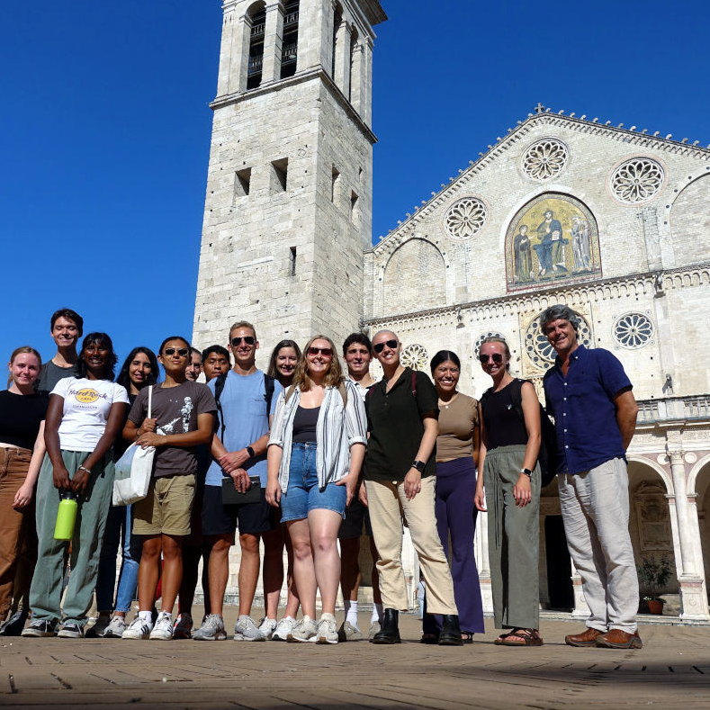 large group posing in front of a historic looking structure