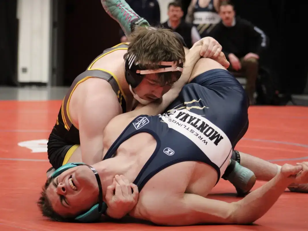 Man in black and gold uniform wrestling man in blue uniform.