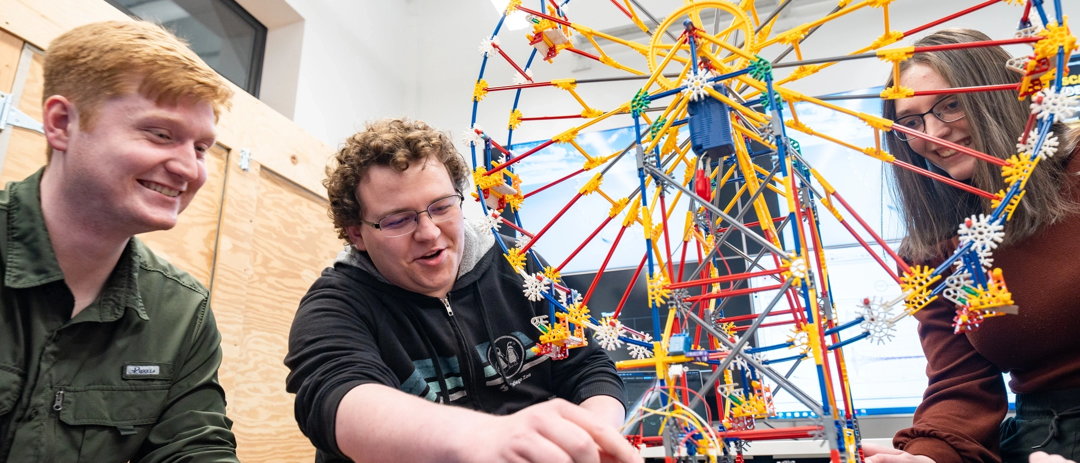 Photos of upcoming graduates in the cyber security program showing off a model ferris wheel which replicates how a cyber attack could affect mechanical processes.
