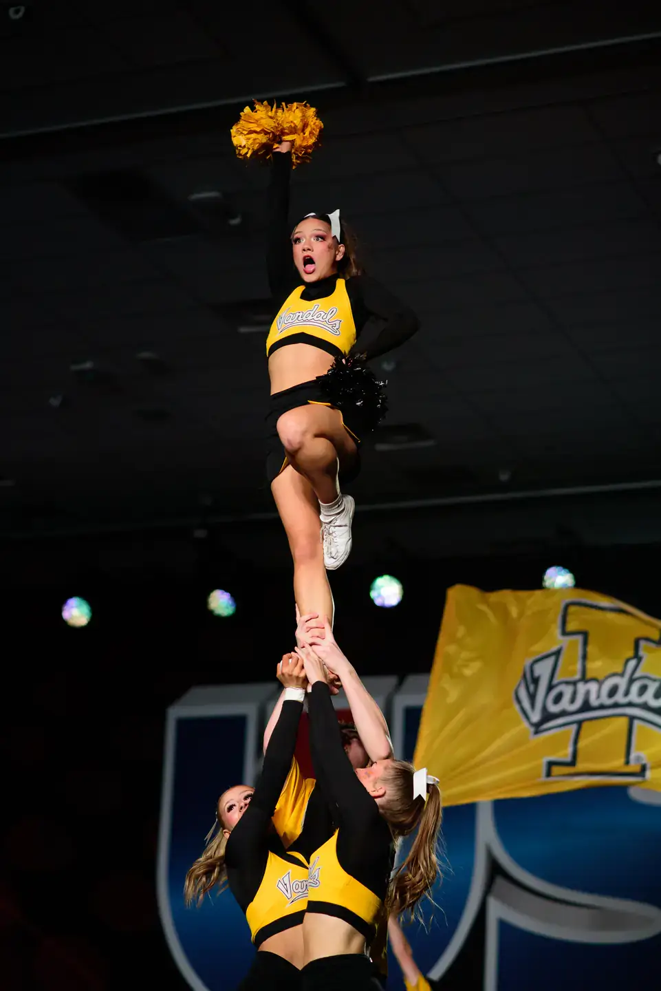 Three women in black and yellow Vandal uniforms performing a cheer.