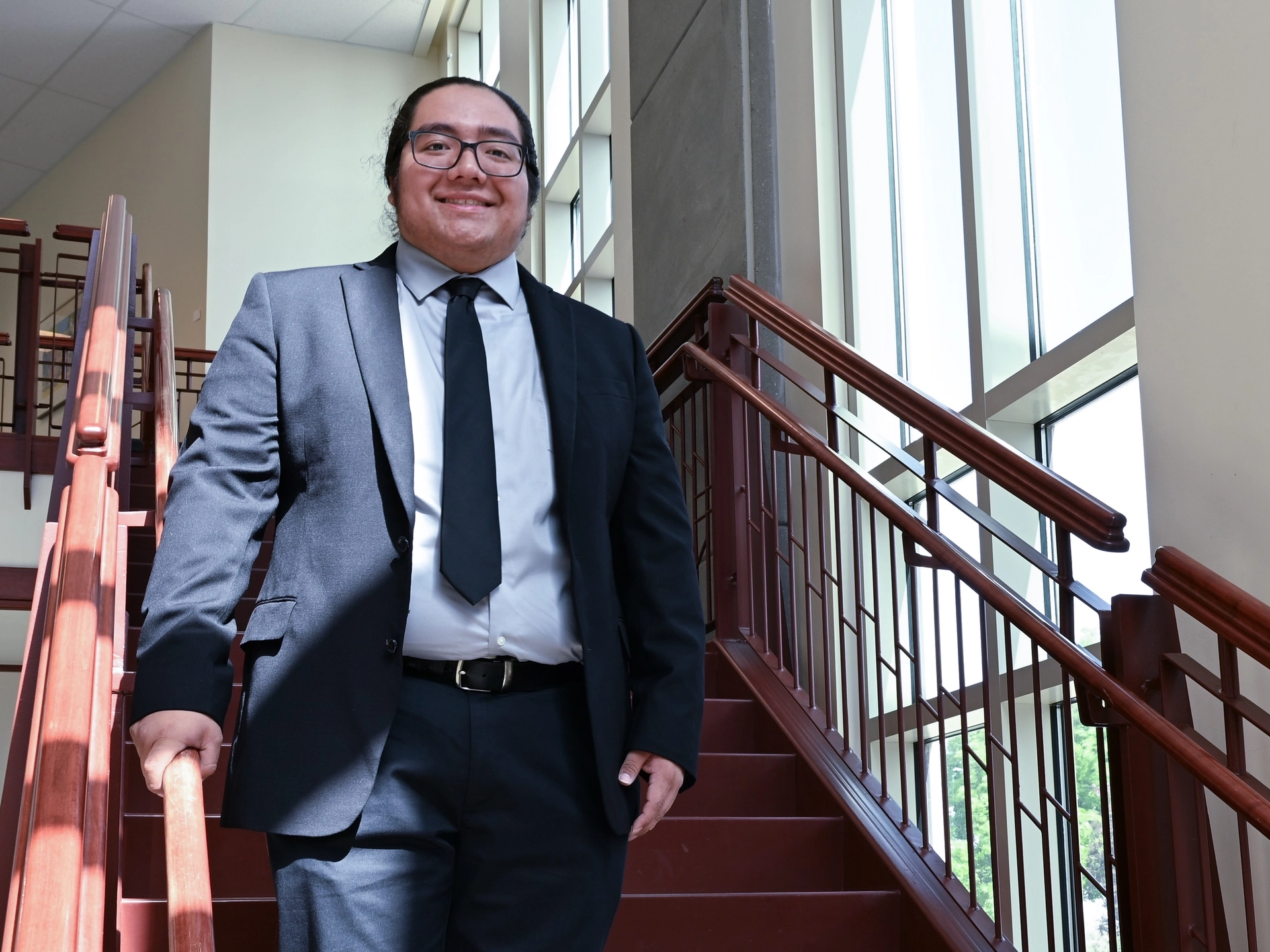 Smiling man wearing suit and tie stands on staircase.