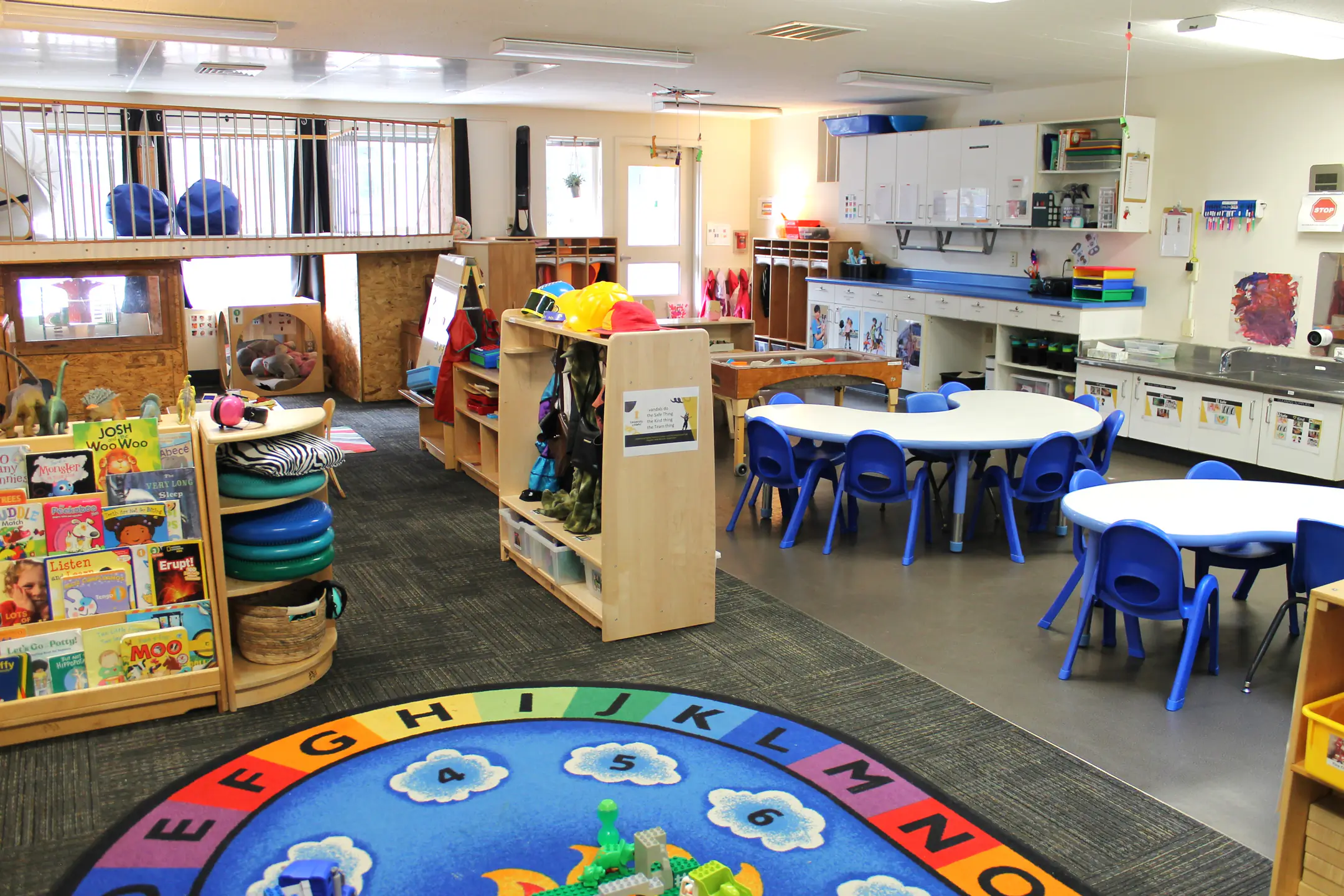 A large classroom with group tables, reading corner, and play rug.