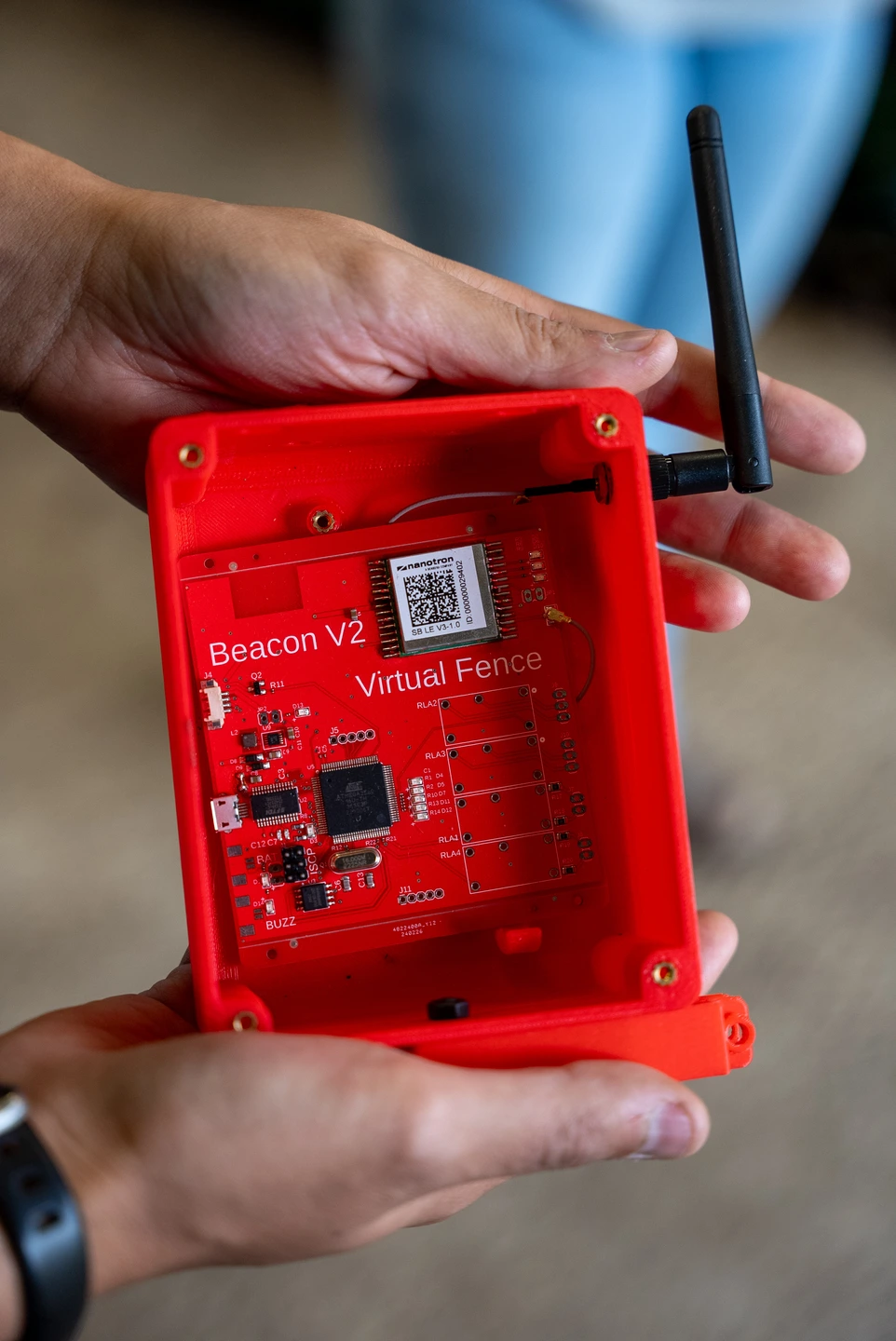 Two hands hold a red radio beacon for the Virtual Fence.
