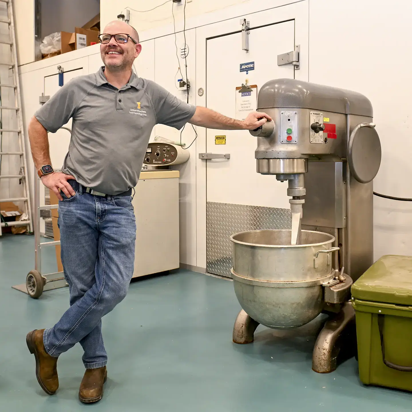 A person leaning on a large industrial mixer in a laboratory or food processing setting.