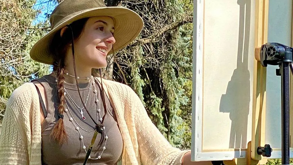 Closeup of woman painting with trees in background.