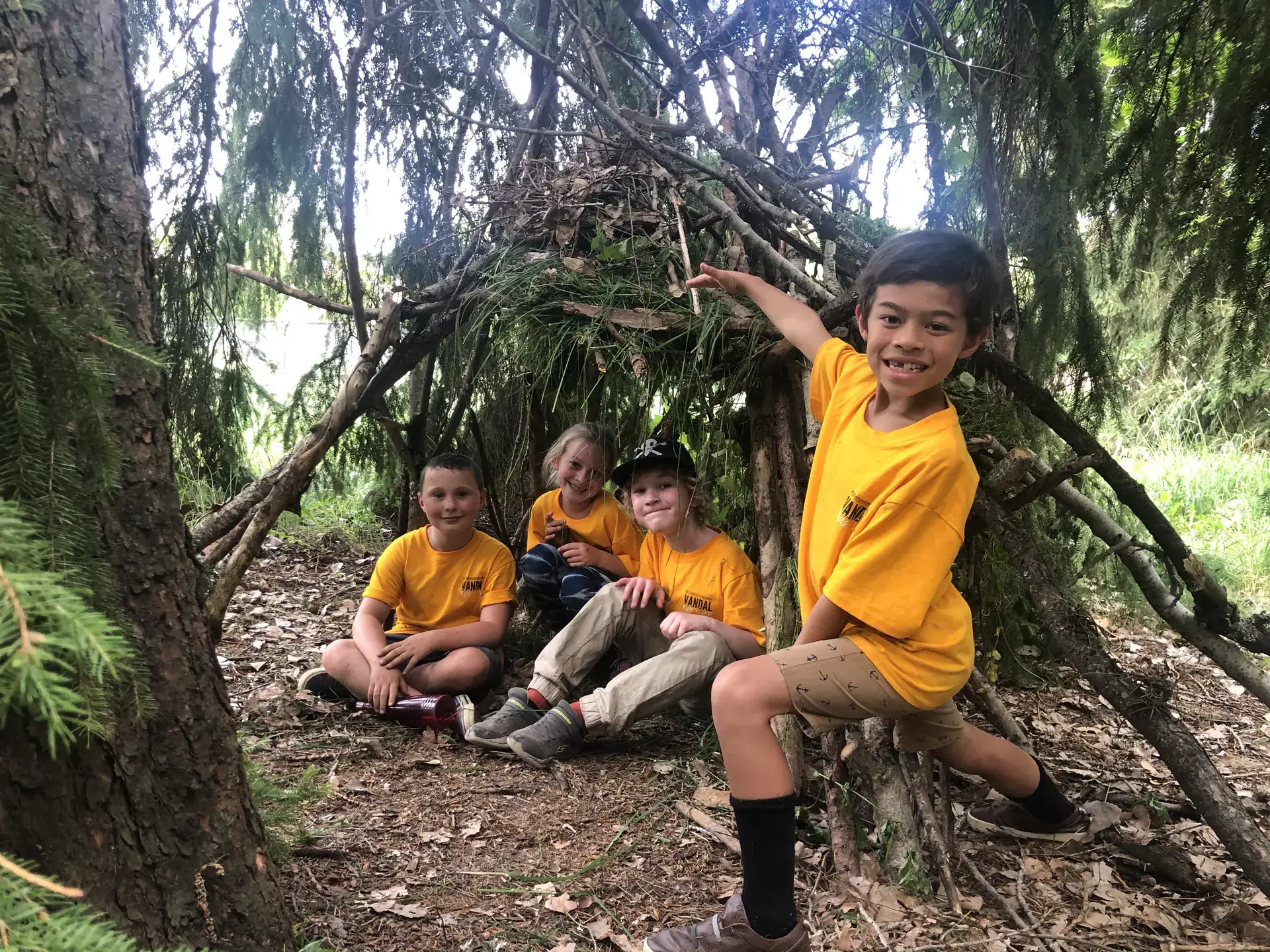 Four kids smiling in front of a wooden fort