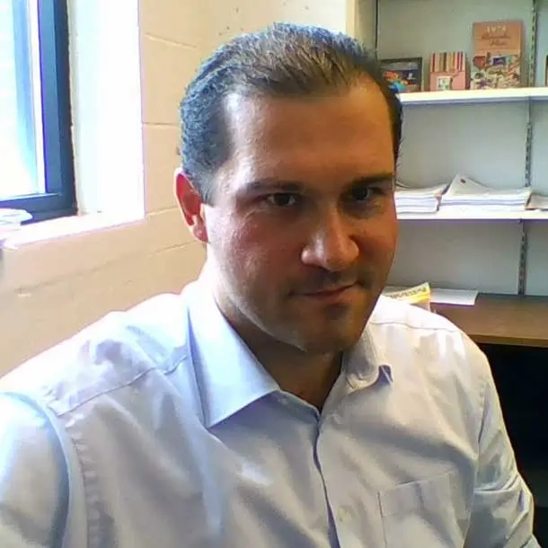 A man smiling in front of his office desk