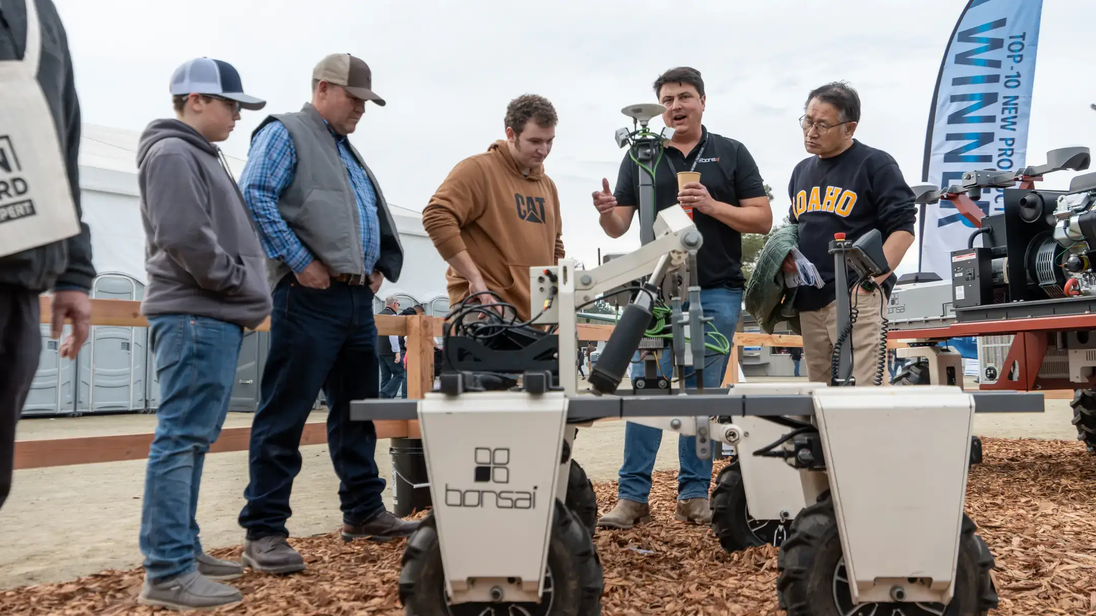 Several people stand near farm machinery as one person leads a discussion.