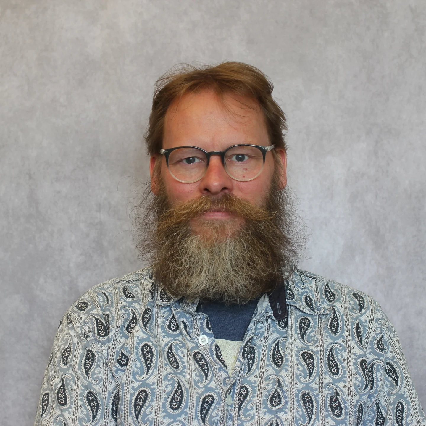 Portrait of a man standing in front of a grey backdrop.