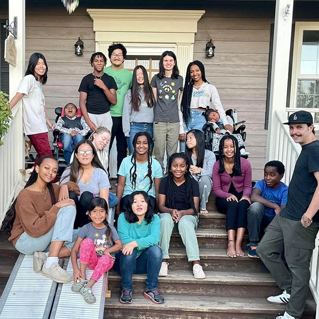 A large group of smiling people gathered on the stairs of a porch.
