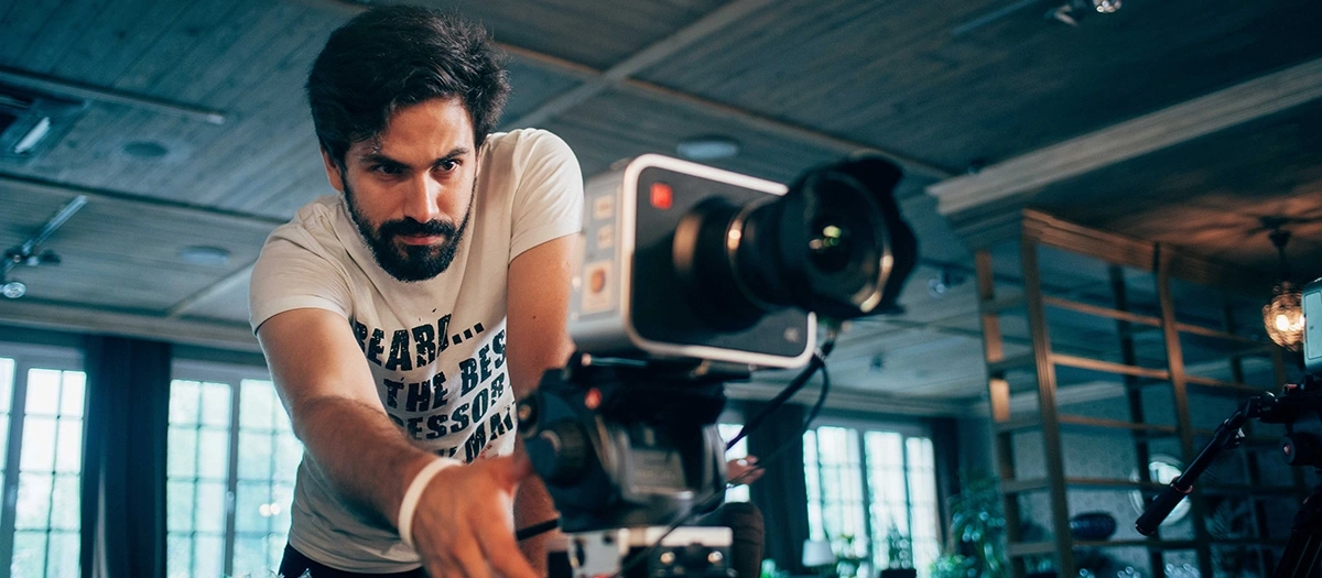 Man with a beard operates a video camera.