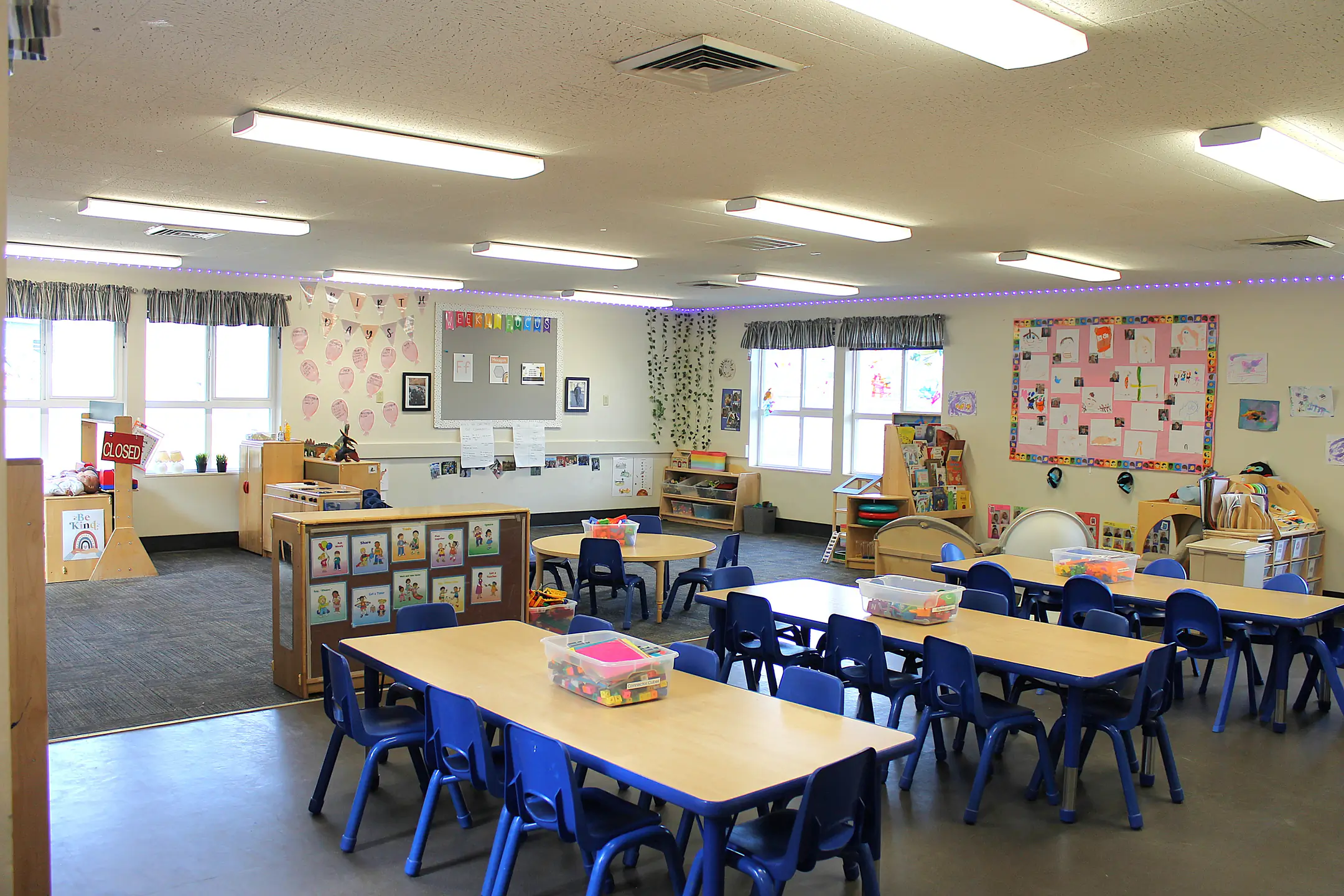 A classroom with group tables, reading corner, and play area.