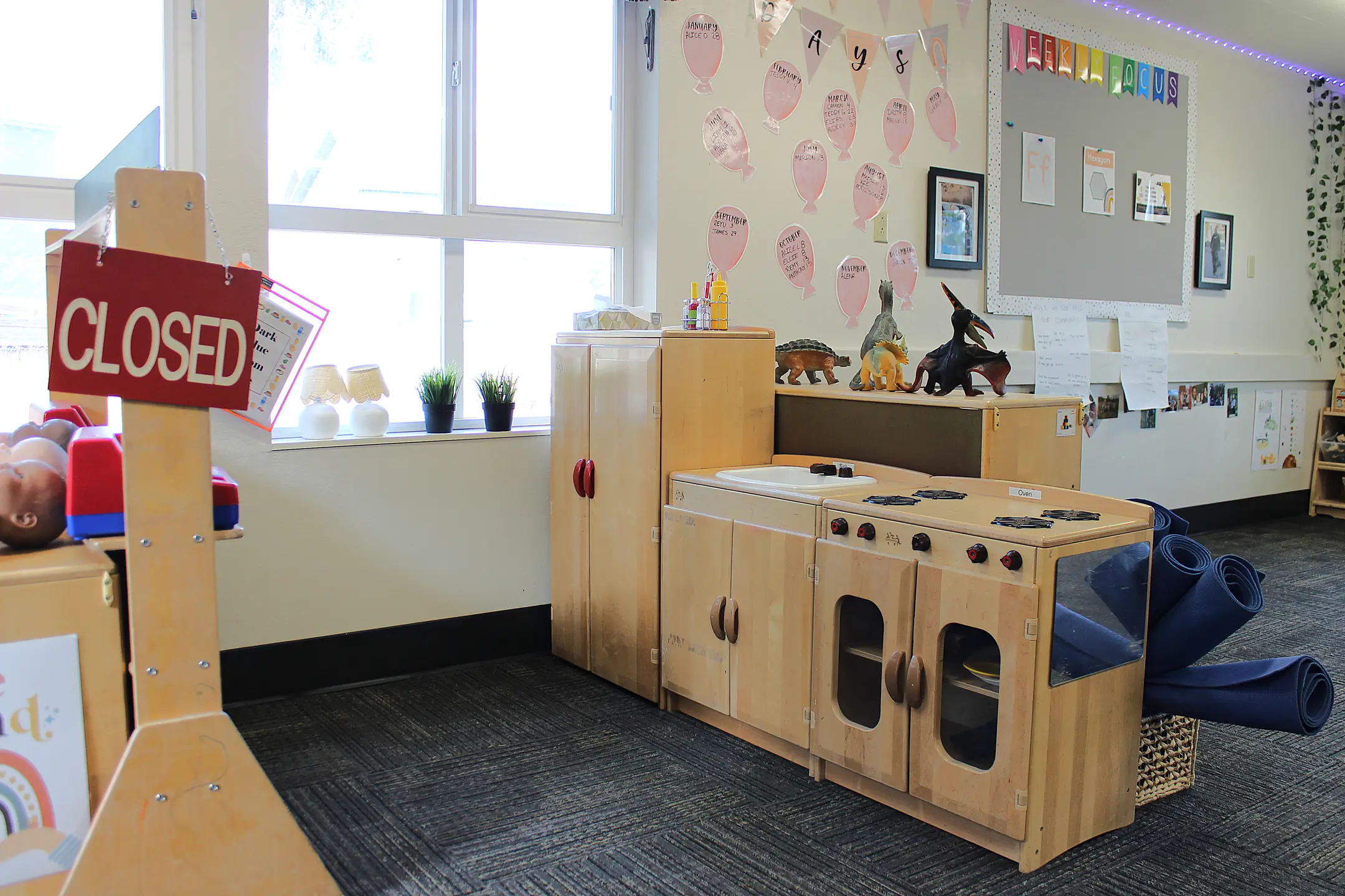 A play area with wooden toy kitchen, play mats, and small dinosaur figurines.