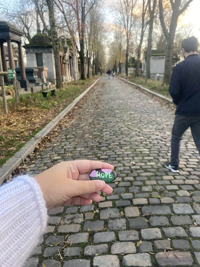 A hand holding a rock painted with hearts and the name Hope