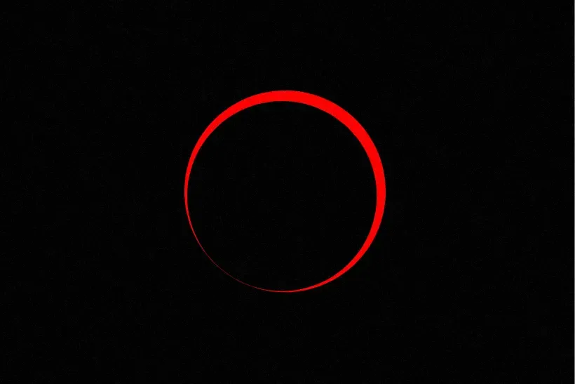 A red halo of the sun silhouetted around the moon, surrounded by blackness, during a solar eclipse.