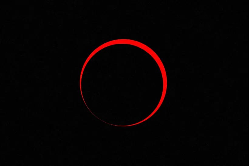 A red halo of the sun silhouetted around the moon, surrounded by blackness, during a solar eclipse.
