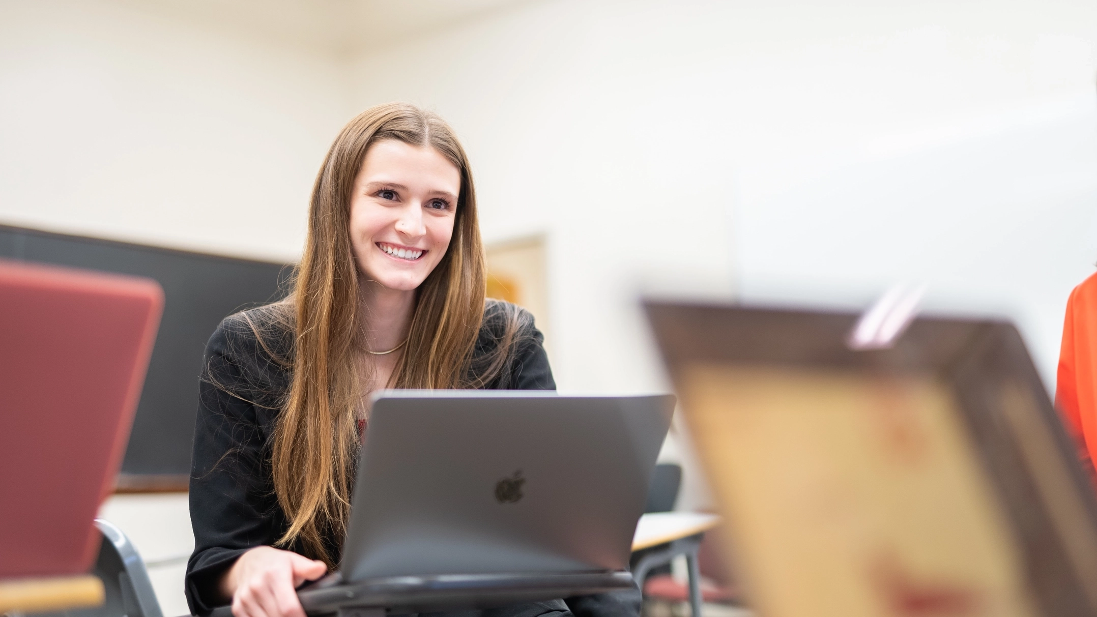 A smiling student sits at a desk with a laptop.