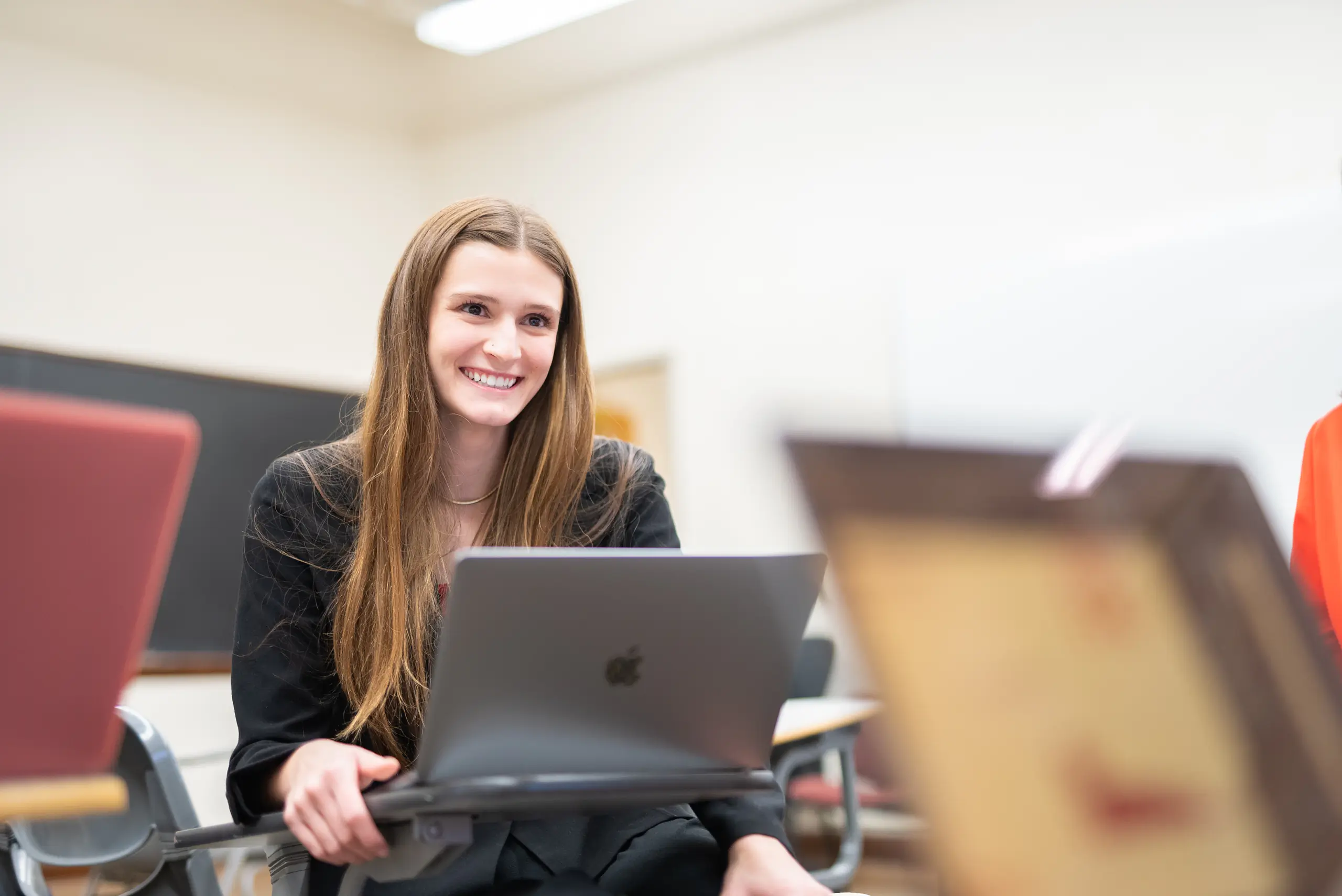 A smiling student sits at a desk with a laptop.