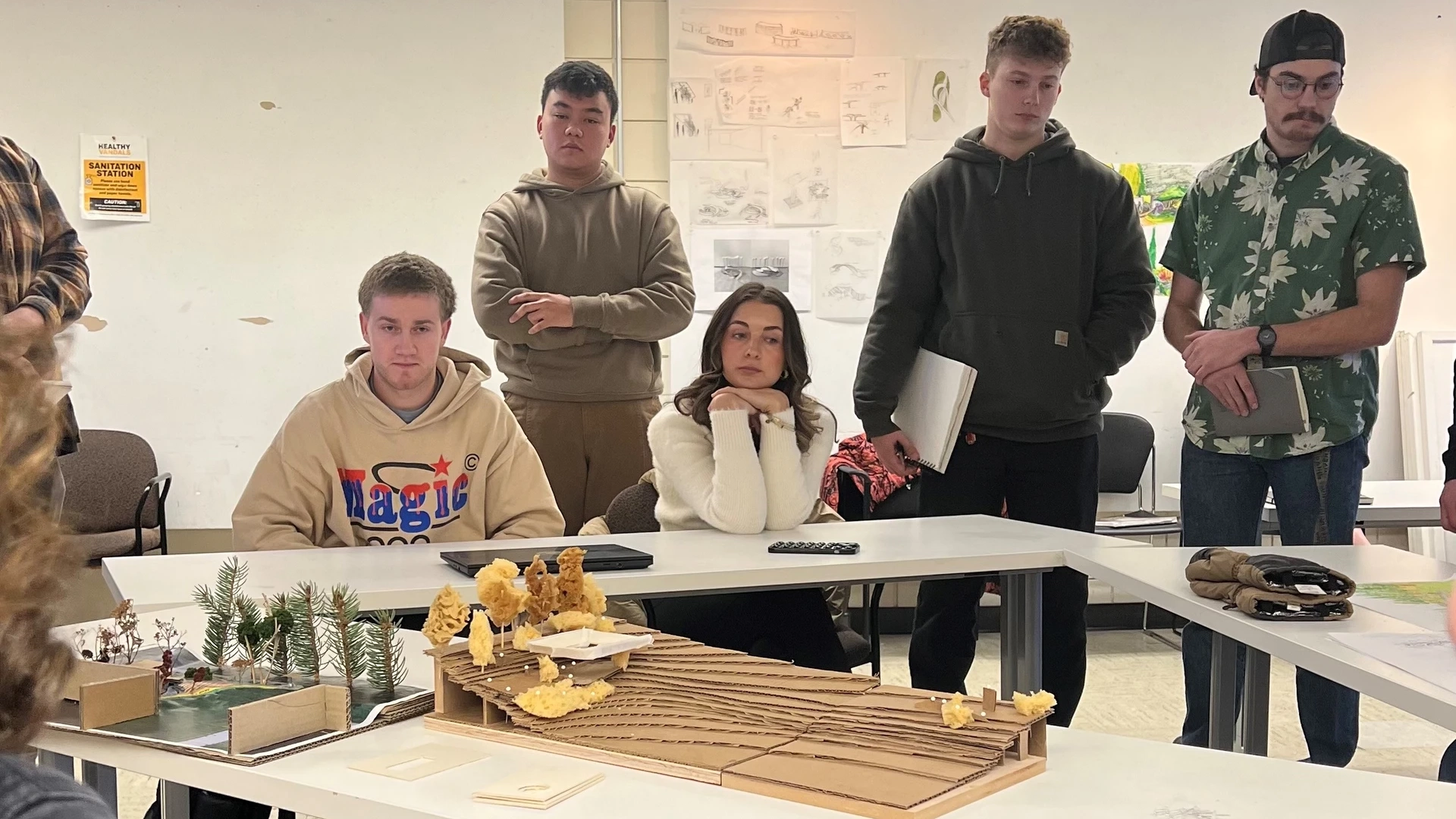 Photo of three people standing and two people sitting around a table