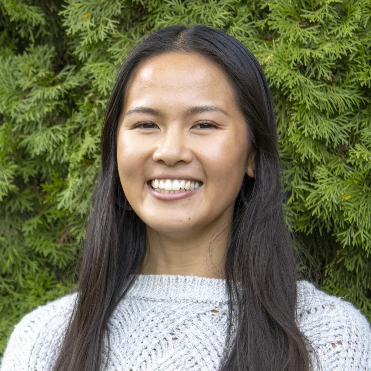 A woman with dark brown hair in a sweater smiling at the camera