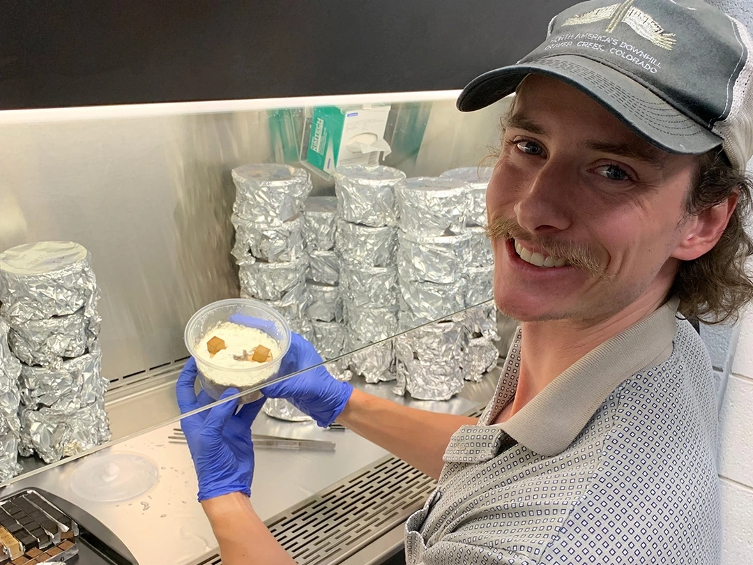 A man holds up a microbial sample under a chemical hood.