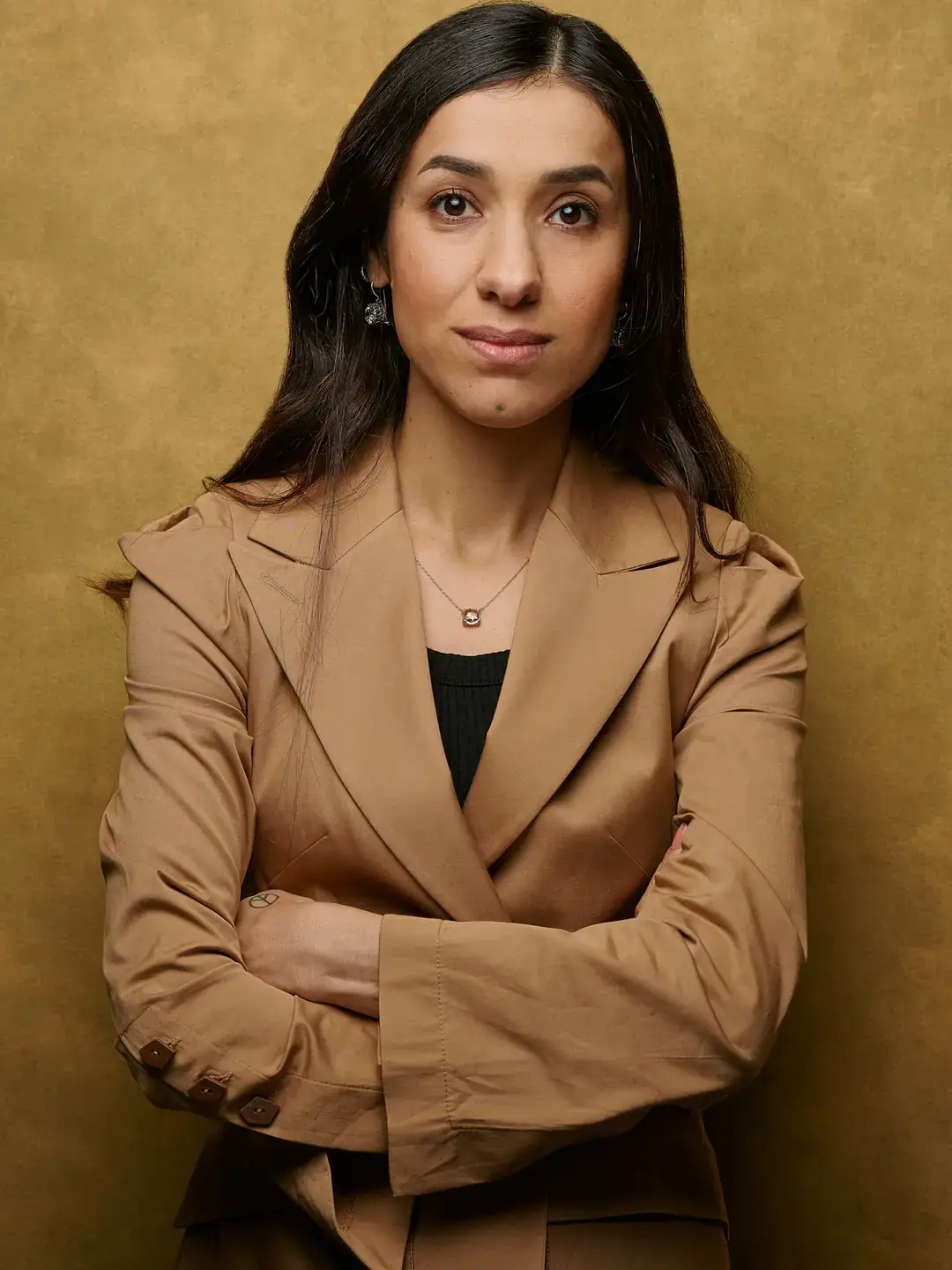 Headshot of Nadia Murad standing against a golden brown backdrop.